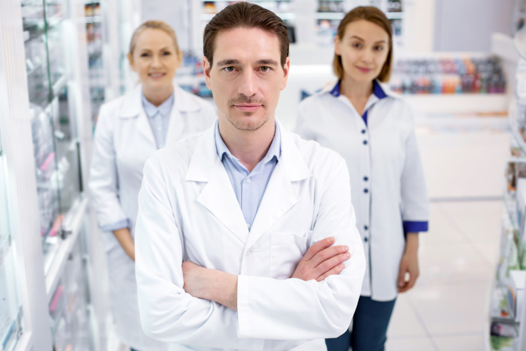 Work,Duty.,Successful,Three,Pharmacists,Looking,At,Camera,While,Staying